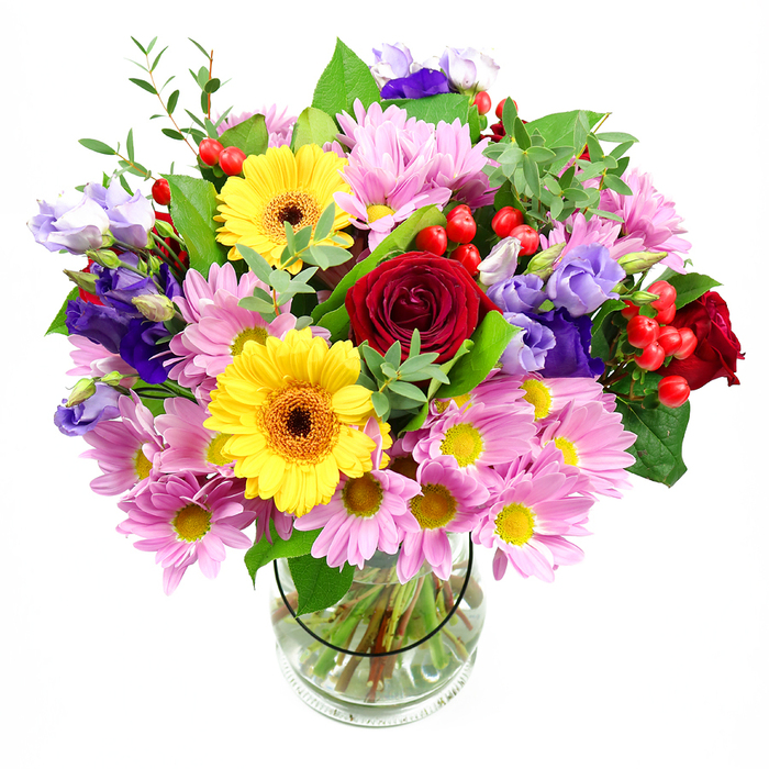 In this image, a substantial mixed bouquet is displayed in a transparent glass vase, its rounded form set crisply against a pure white background that highlights every detail. The eye is first drawn to the cluster of deep red roses at the centre; their plush, velvety petals spiral inward with a richness that suggests devotion and sincerity. Just beside them, two radiant yellow gerbera daisies, each with a distinct dark brown-orange centre, radiate cheerful energy, like small bursts of sunshine on a Bayswater morning. Surrounding these central flowers, a lush ring of soft pink daisies or chrysanthemums cascades outward, their many slender petals and bright yellow eyes creating a sense of lightness and cushion-like softness. Threaded among the pink daisies are refined purple and lavender lisianthus, their slightly ruffled, bell-shaped blooms contributing an air of modern elegance and a cool counterpoint to the warmer reds and yellows. Dotted throughout are bright red hypericum berries, each smooth and round, adding a playful texture and a hint of contemporary design. A tapestry of foliage in deep and mid-green tones provides structure and depth, from wide, glossy leaves to fine, airy sprigs, reminiscent of the layered greenery in nearby Kensington Gardens. The stems are clearly visible through the vase, neatly cut and arranged in fresh water, a subtle sign of professional care. The bouquet feels like it has been crafted for joyful occasions across Bayswater-perhaps to brighten a breakfast table off Queensway, to celebrate good news in a flat near Royal Oak, or to bring a burst of garden colour into a calm, white interior-radiating warmth, freshness, and the quiet artistry of an experienced local florist.